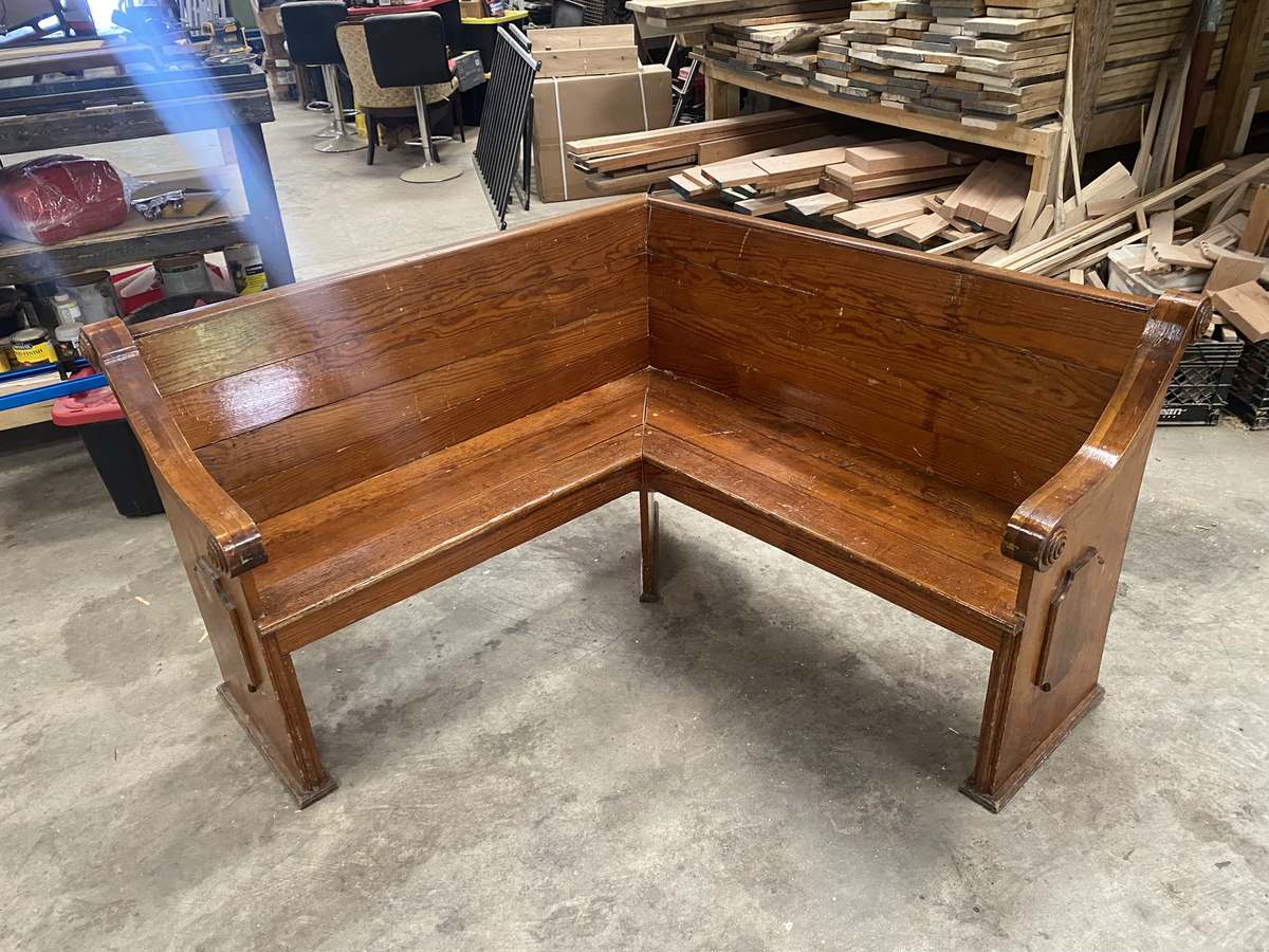 An antique church pew reshaped into an L-shaped corner seat, its original carved scroll ends at both outer ends