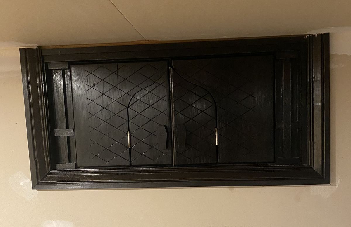 A carved shutter assembly fitted over an interior window, its two doors closed and carved with a diamond lattice inside a molded surround